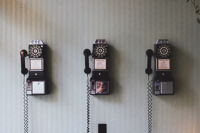 Three vintage wall-mounted rotary telephones beneath a ‘Local calls 10¢’ sign — West Michigan Web contact hero background